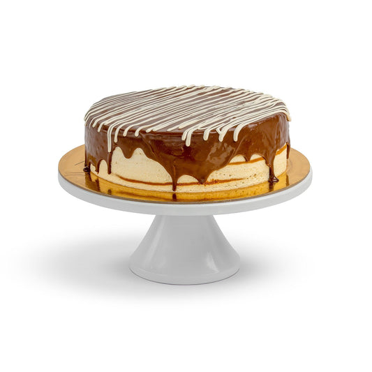 A whole Birdie cake displayed on a white cake stand, featuring layers of honey cake topped with caramel glaze and white chocolate drizzle.