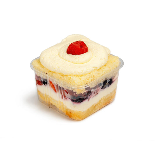 Open Berry Cake Cup displaying vibrant layers of vanilla sponge, fresh berries, and cream, topped with a swirl of frosting and a single raspberry garnish.