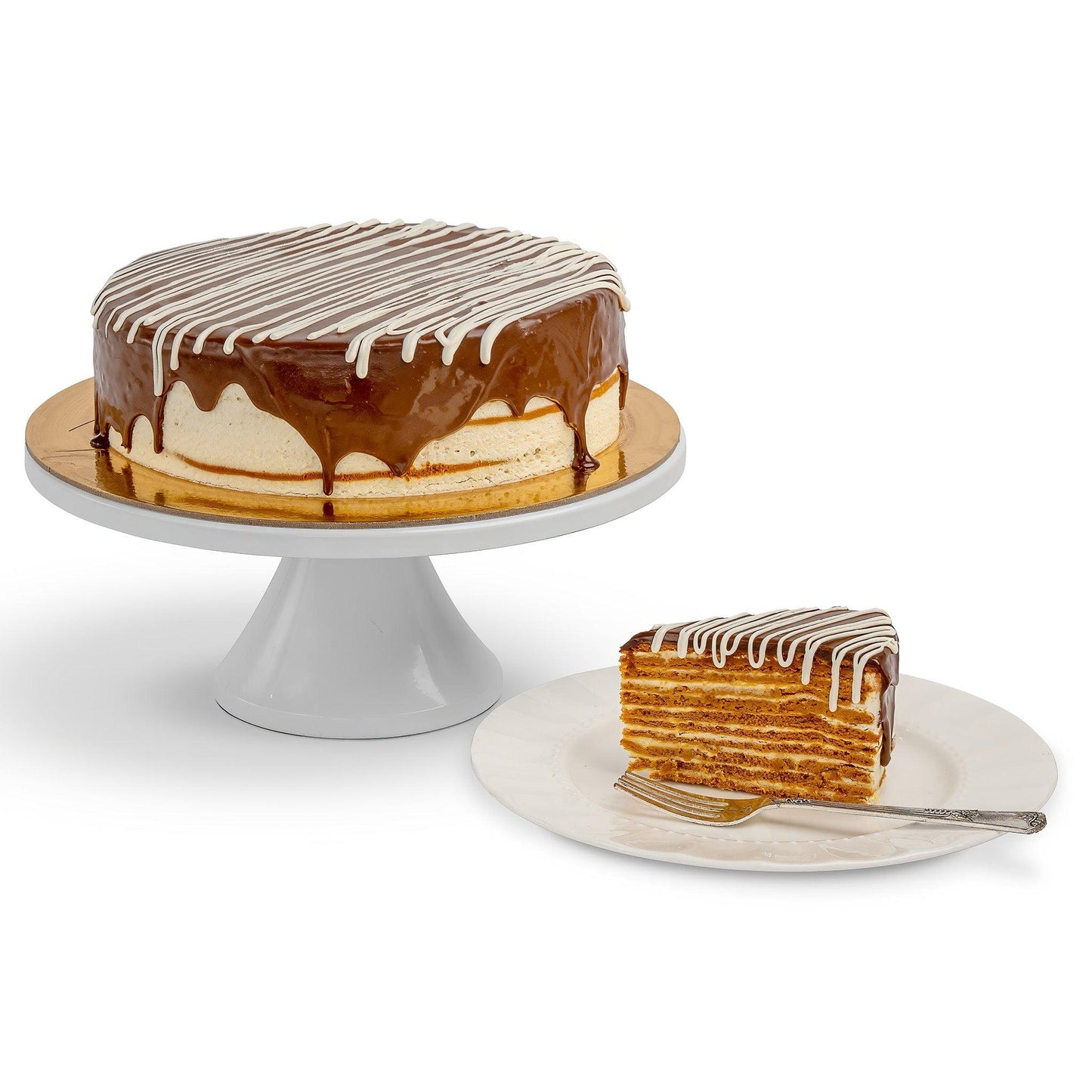 A Birdie cake on a cake stand, with a slice served on a plate, showcasing its rich, golden layers of honey cake, caramel glaze, and white chocolate drizzle.