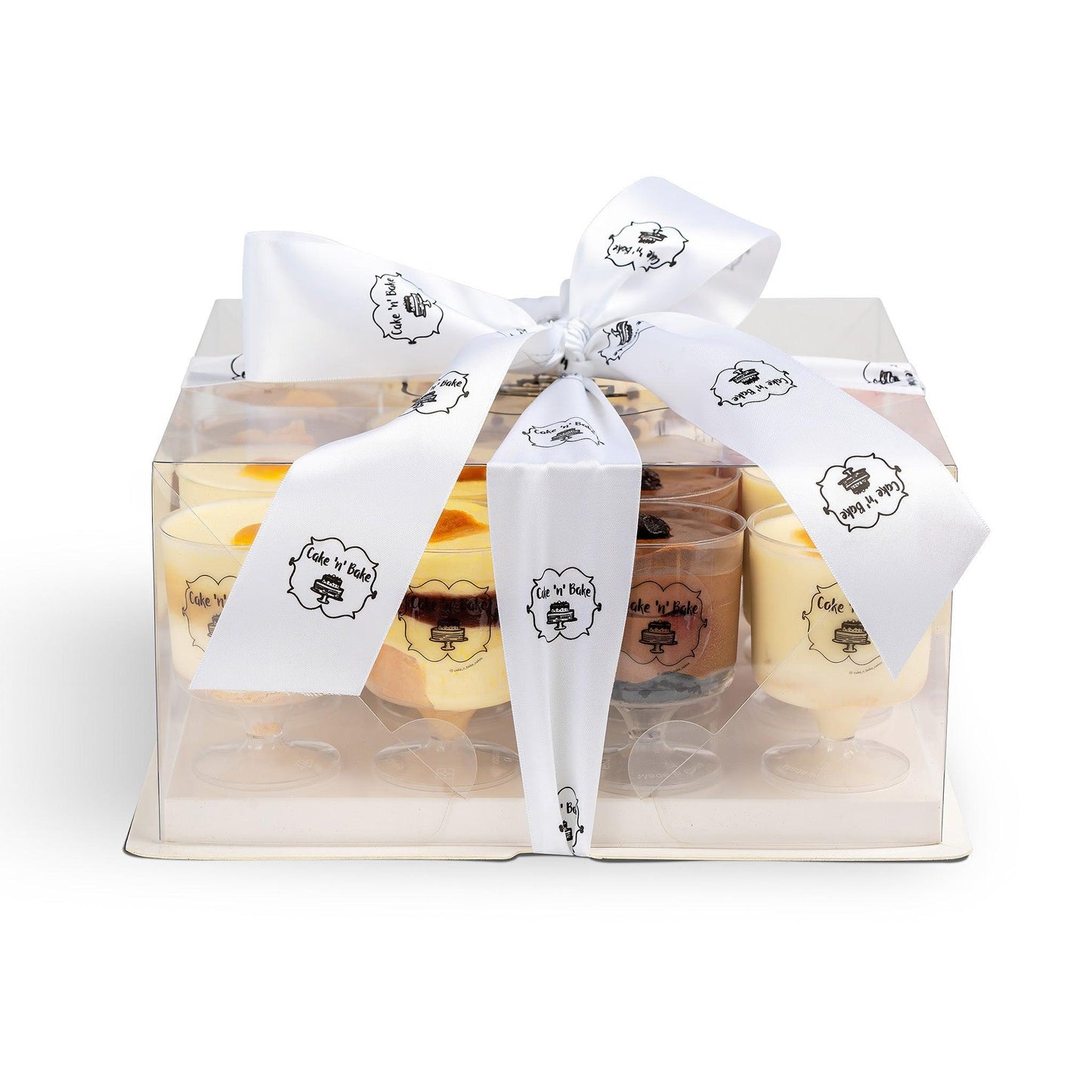 A beautifully packaged gift box featuring 16 servings of assorted mousse desserts, wrapped with a white satin ribbon adorned with the Cake N’ Bake logo, perfect for gifting or special occasions.