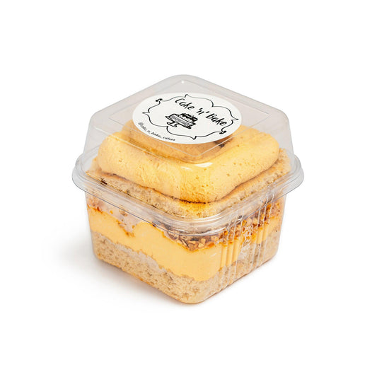 Vanilla-Crunchy Hazelnut Cake Cup in a clear container with the Cake Nā Bake logo, featuring rich layers of vanilla cake and hazelnut frosting.